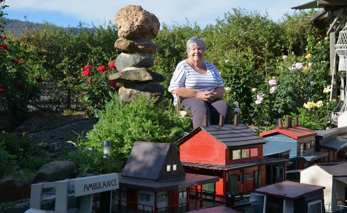 LABOUR OF LOVE: Robin Stanford sitting in the centre of the rose garden and railway display that her husband Colin Stanford has extended across the whole of his backyard for 2017's Model Train Festival.