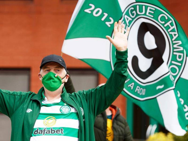 A Celtic fan with a protective mask celebrates Celtic's ninth-straight title outside their stadium
